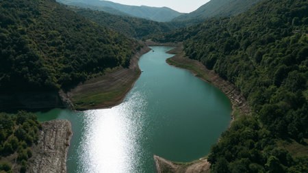 Aerial view of Zavoj Lake in Stara Planina National Park, Serbia, with water reflecting sunlight between green forested hillsの写真素材