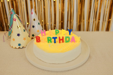 Birthday cake with colorful candles and party hats on the table with golden festive background