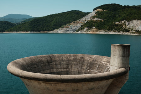 Close view of the circular spillway at Rovni Lake in Serbia, with vivid turquoise water and forested hillsの写真素材