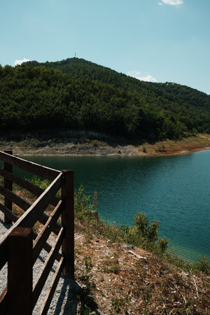Wooden fence near the turquoise water of Rovni Lake in Serbia, with green forested hills under a clear skyの写真素材