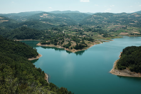 Beautiful aerial perspective of Rovni Lake in Serbia, with emerald water and forested shoreline. Surrounded by green hills and villagesの写真素材