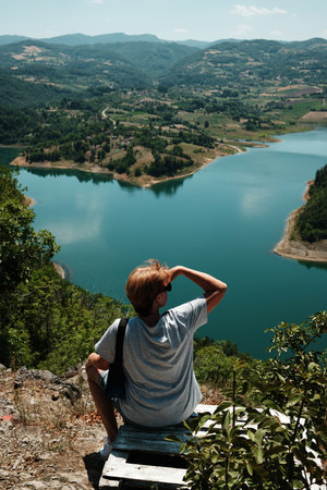 Woman sitting above Rovni Lake in Serbia, admiring the panoramic mountain scenery. Rear view. Travel...