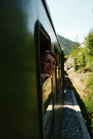 Happy smiling woman looking out of a vintage green train window during a scenic ride through Mokra Gora. Sargan Eight - a popular tourist destination in Serbiaの写真素材
