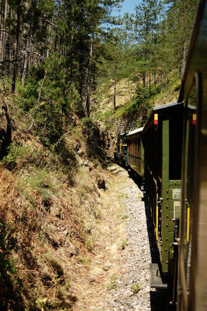 Vintage green train traveling through a narrow rocky pass surrounded by steep cliffs and forest in Mokra Gora. Sargan Eight - a popular tourist destination in Serbiaの写真素材