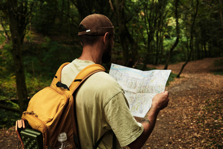 Man with backpack reading a map in Fruska Gora National Park, Serbia. Exploring hiking trail in forest. Rear viewの写真素材