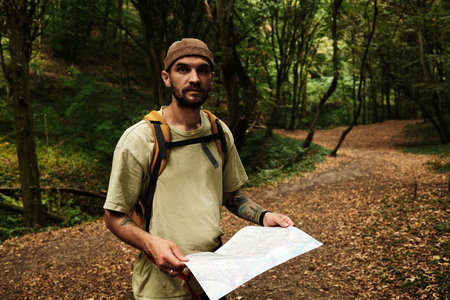 Man with backpack reading a map in Fruska Gora National Park, Serbia. Exploring hiking trail in forest. Front view portraitの写真素材
