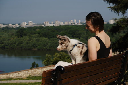Woman with border collie puppy sitting on wooden bench in Kalemegdan Fortress, Belgrade, overlooking the Sava Riverの写真素材