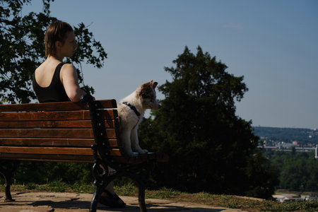 Smiling young woman with her puppy sitting on a bench with city view in backgroundの写真素材
