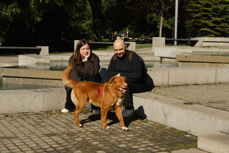 Couple with Nova Scotia Duck Tolling Retriever relaxing by fountain in Belgrade park on sunny dayの写真素材