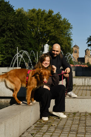 Couple relaxing by fountain with Nova Scotia Duck Tolling Retriever in Belgrade city park. Walking with dog conceptの写真素材