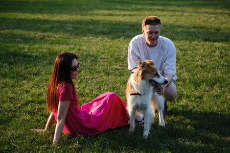 Young couple relaxing on the grass with their mix breed dog in the park at golden hour. Pets, love, and lifestyle outdoors concept.の写真素材