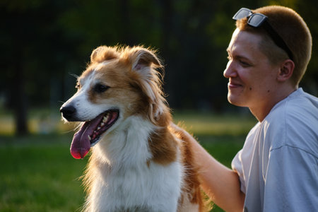Young man smiling while petting his dog outdoors in the park at sunset. Friendship and love with pets conceptの写真素材