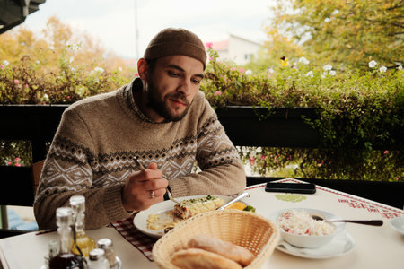Man in sweater enjoying lunch with bread and salad at an outdoor restaurant during autumn day, cozy and relaxed dining atmosphereの写真素材