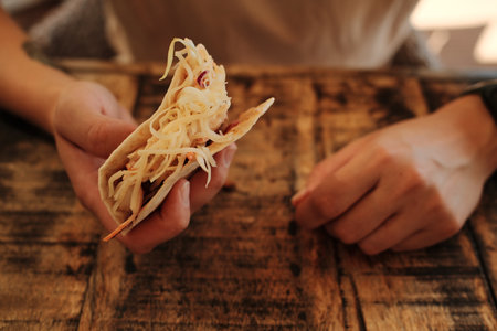 Close-up of woman holding a cheesy taco with both hands at a rustic wooden tableの写真素材