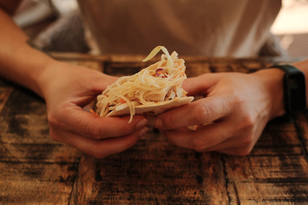 Close-up of woman holding a cheesy taco with both hands at a rustic wooden table