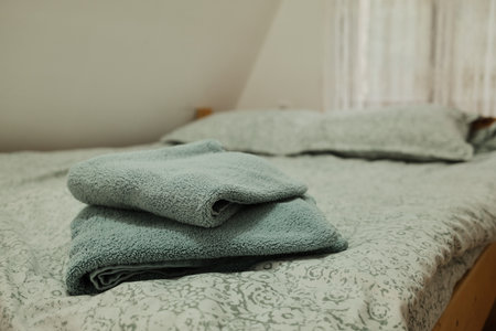 Folded soft towels placed on a neatly made bed with patterned linen and natural light through a lace...