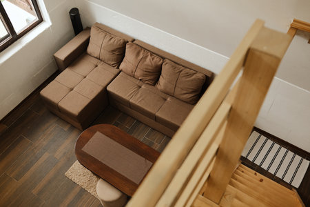 Minimalist living room interior with a brown sectional sofa, wooden stairs and warm natural tones....