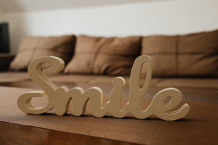 Close up of wooden Smile sign on a brown table in front of a soft sofa. Perfect for lifestyle, home decor, and positivity themed projectsの写真素材
