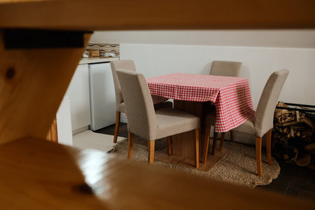 Rustic dining setup with beige chairs and red checkered tablecloth in a small kitchen corner. Ideal for home, lifestyle, and hospitality conceptsの写真素材