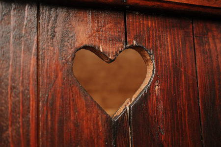 Detailed view of a wooden heart cutout on an aged dark wood surface. Ideal for design, craft, and emotional rustic lifestyle visualsの写真素材
