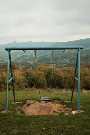 Lonely swing on a hill overlooking scenic mountain valley and forest under cloudy sky. Ideal for travel, childhood, and mindfulness conceptsの写真素材