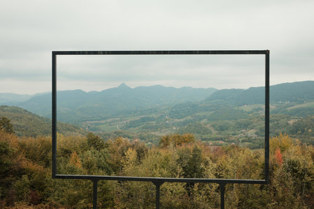 Large metal frame placed on hill framing panoramic mountain landscape and forest. Perfect for...