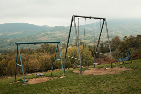 Multiple swings placed on a hill with a panoramic view of mountains and valleys under cloudy sky. Ideal for travel, recreation, and freedom conceptsの写真素材