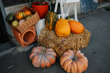 Colorful pumpkins arranged on a hay bale beside a street shop create a cozy autumn atmosphere perfect for seasonal decoration or harvest themesの写真素材