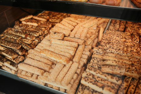 Various crunchy pastry sticks topped with sesame and seeds displayed in bakery showcase