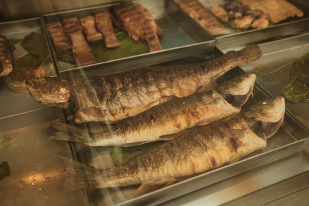 Grilled whole fish arranged on metal tray in restaurant kitchen showcase