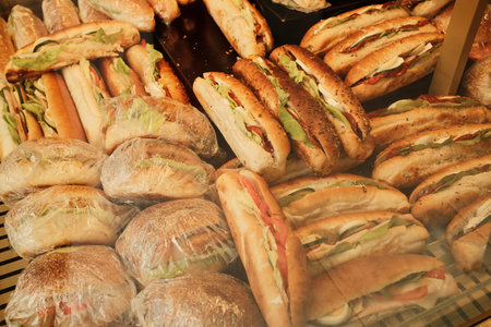 Variety of sandwiches with lettuce, tomato, egg, and cheese wrapped and displayed in bakeryの写真素材