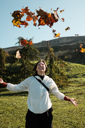 Smiling woman throws colorful autumn leaves into the air on a sunny dayの写真素材