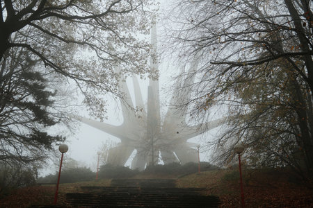 Mysterious view of the Kosmaj Monument rising through dense fog, surrounded by autumn trees and...