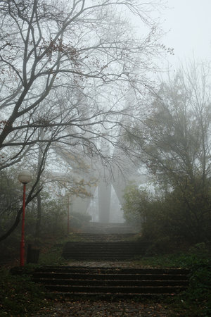 Mysterious view of the Kosmaj Monument rising through dense fog, surrounded by autumn trees and quiet forest atmosphereの写真素材