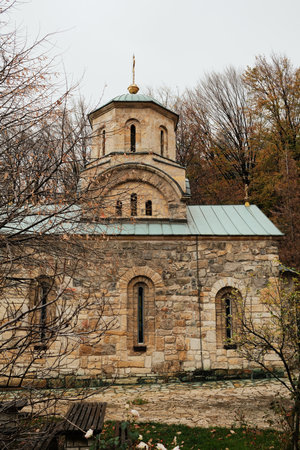 Stone dome with golden cross rising above monastery roof among bare autumn trees. Monastery Tresije, Serbiaの写真素材