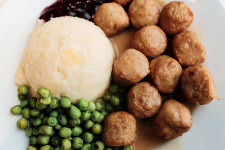 Plate of classic Swedish meatballs served with mashed potatoes, green peas, gravy, and lingonberry sauce. Comforting homemade meal with Scandinavian flavor.の写真素材