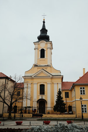 A yellow baroque church in Sremski Karlovci, Serbia, with an arched entrance and quiet courtyard. A...