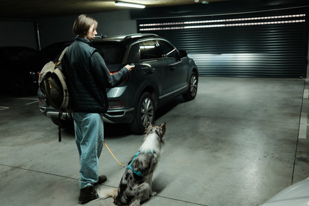 A woman stands in an underground garage with her dog, holding a car key near a parked vehicle. The scene shows preparation for driving, pet travel, and everyday urban mobilityの写真素材