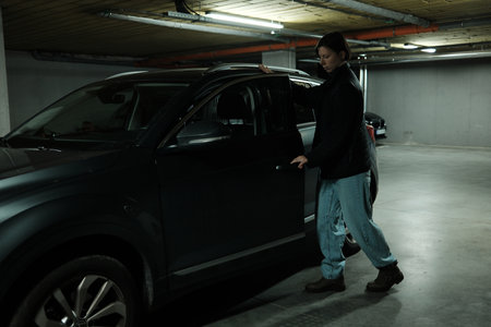 A woman opens the door of a parked vehicle in an underground garage, preparing for a city commute. The scene highlights modern urban lifestyle and mobilityの写真素材