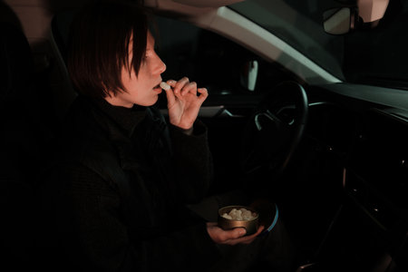 A woman sits in the drivers seat holding a tin of candies and eating one during a quiet pause. The image reflects rest, comfort, and everyday life on the roadの写真素材