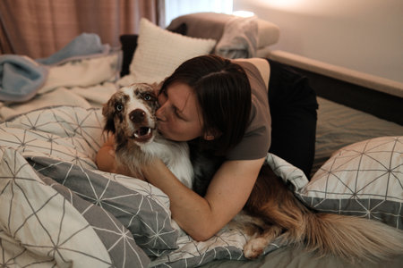 A woman embraces a border collie on the bed and kisses the dog on the cheek. The moment represents affection, trust, and joyful home lifeの写真素材