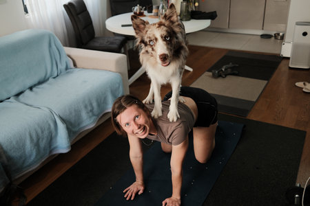 A woman kneels on a mat while a border collie stands on her back. The moment captures energy, humor, and the strong bond between themの写真素材