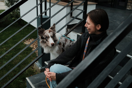 The Border Collie turns toward the woman while they rest on the stairs. The concept shows trust, attention, and emotional communicationの写真素材