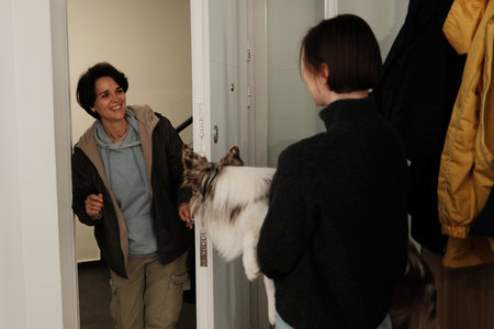 A woman enters the apartment while the border collie watches curiously from her owners arms. The scene conveys welcome and the concept of positive interactionの写真素材