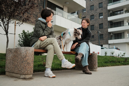Two women sit on a bench with a border collie dog between them. The moment conveys communication and the concept of connectionの写真素材