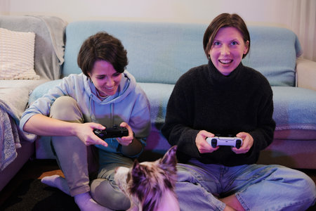 Two women sit on the floor playing a video game while their dog watches closely. The moment captures friendly competition and a cozy, relaxed home moodの写真素材