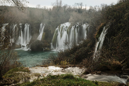 Long exposure view of Kravica Waterfall with smooth flowing water and mist over turquoise river in Bosnia and Herzegovina. Soft motion effect creates calm and atmospheric nature landscapeの写真素材