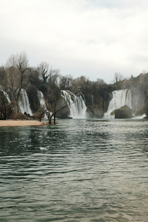 Wide cascading Kravica Waterfall surrounded by forest and turquoise river water in Bosnia and Herzegovina. Natural landscape with flowing streams, mist and calm atmosphere in early springの写真素材