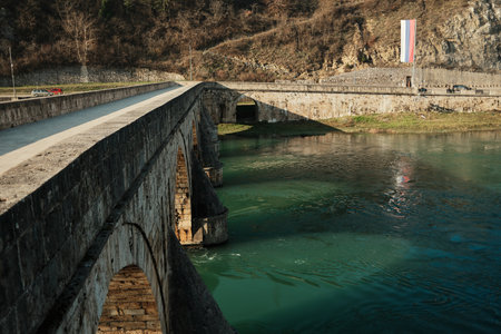 Stone arches of Mehmed Pasha Sokolovic Bridge rise above the green waters of the Drina River in Visegrad. Strong geometry and textures highlight historic engineeringの写真素材