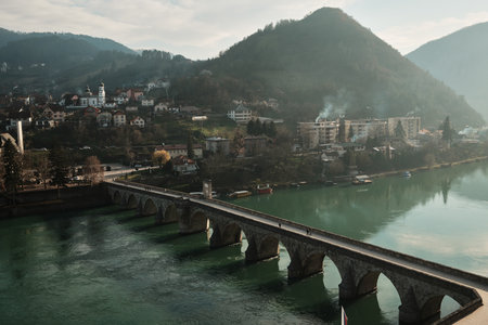 Elevated view shows the historic stone bridge crossing the Drina River with Visegrad town and hills in the background, Bosnia and Herzegovina. Light haze adds depth and atmosphereの写真素材